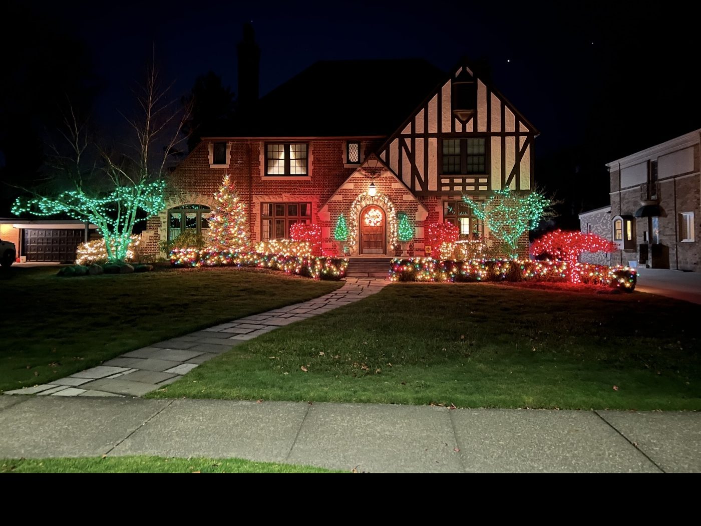 Award-winning Christmas light display on a Tudor home with wrapped trees and lit landscape beds, Balfour St., Grosse Pointe Park