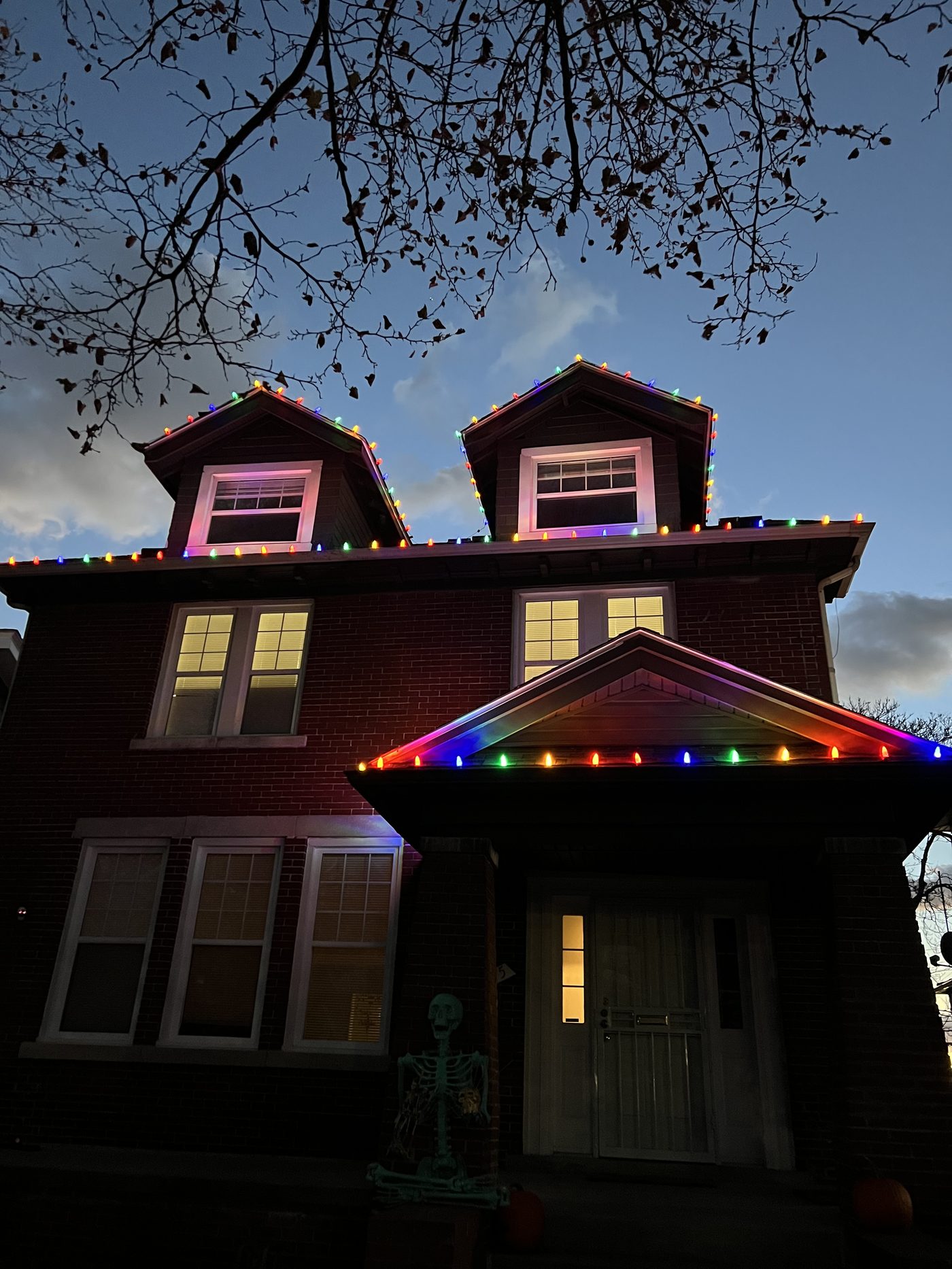 Multicolor C9 bulbs outlining the roofline and two dormers on a brick home in Detroit